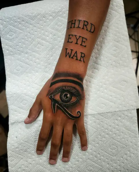 Eye of Horus tattoo with text 'Third Eye War' in black ink on the hand.