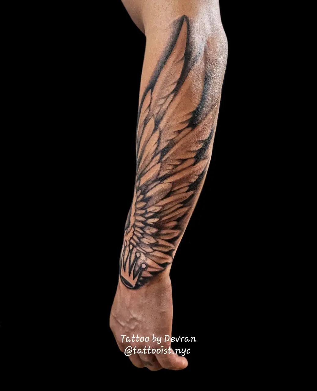 Black and gray wing tattoo with bold airbrush-style shading on the forearm.