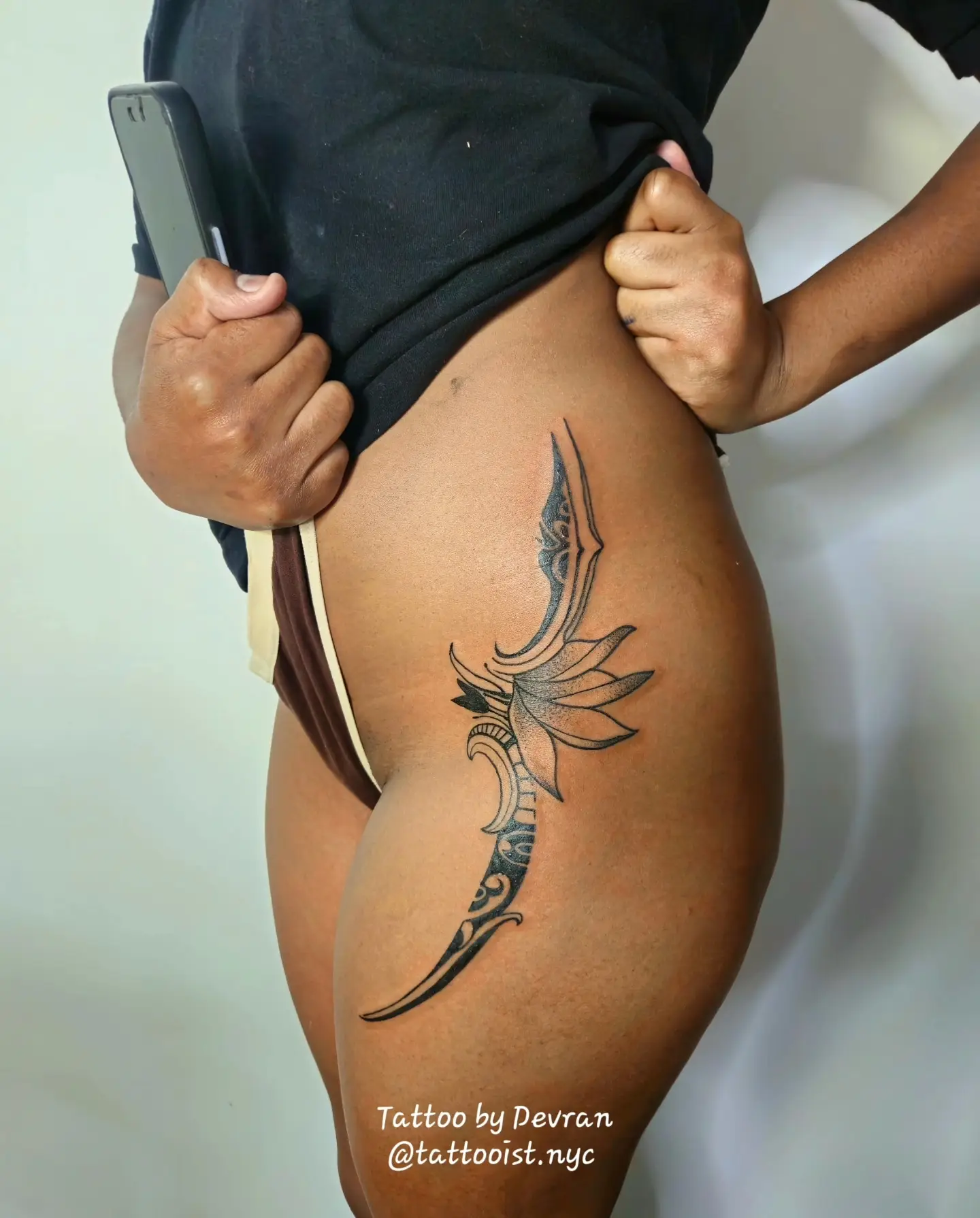 Ornamental dagger and lotus flower tattoo in black ink along the hip and thigh.