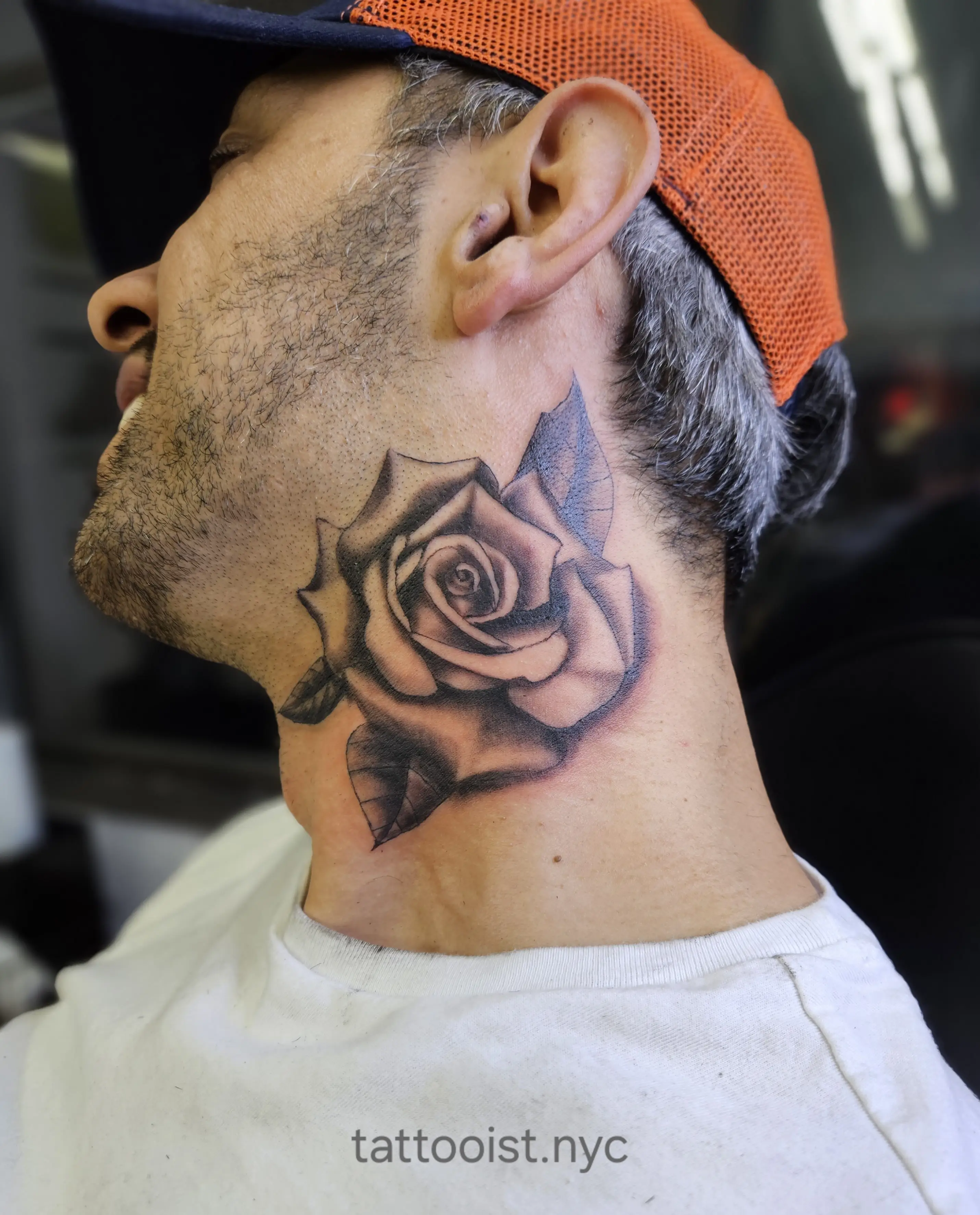 Realistic rose tattoo on the side of the neck in black and gray shading.
