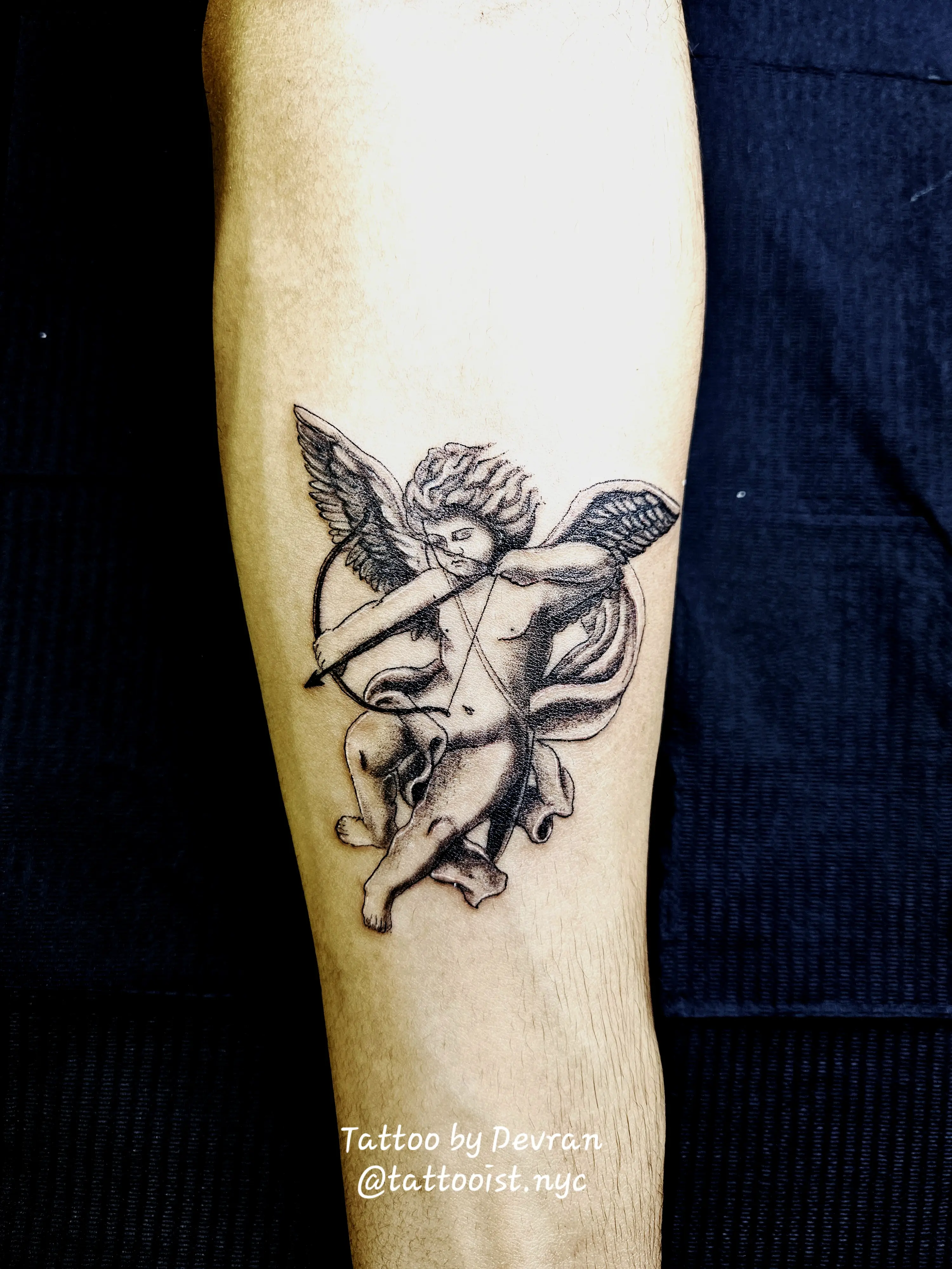 Cherub tattoo holding a bow and arrow, rendered in classical black and gray style.