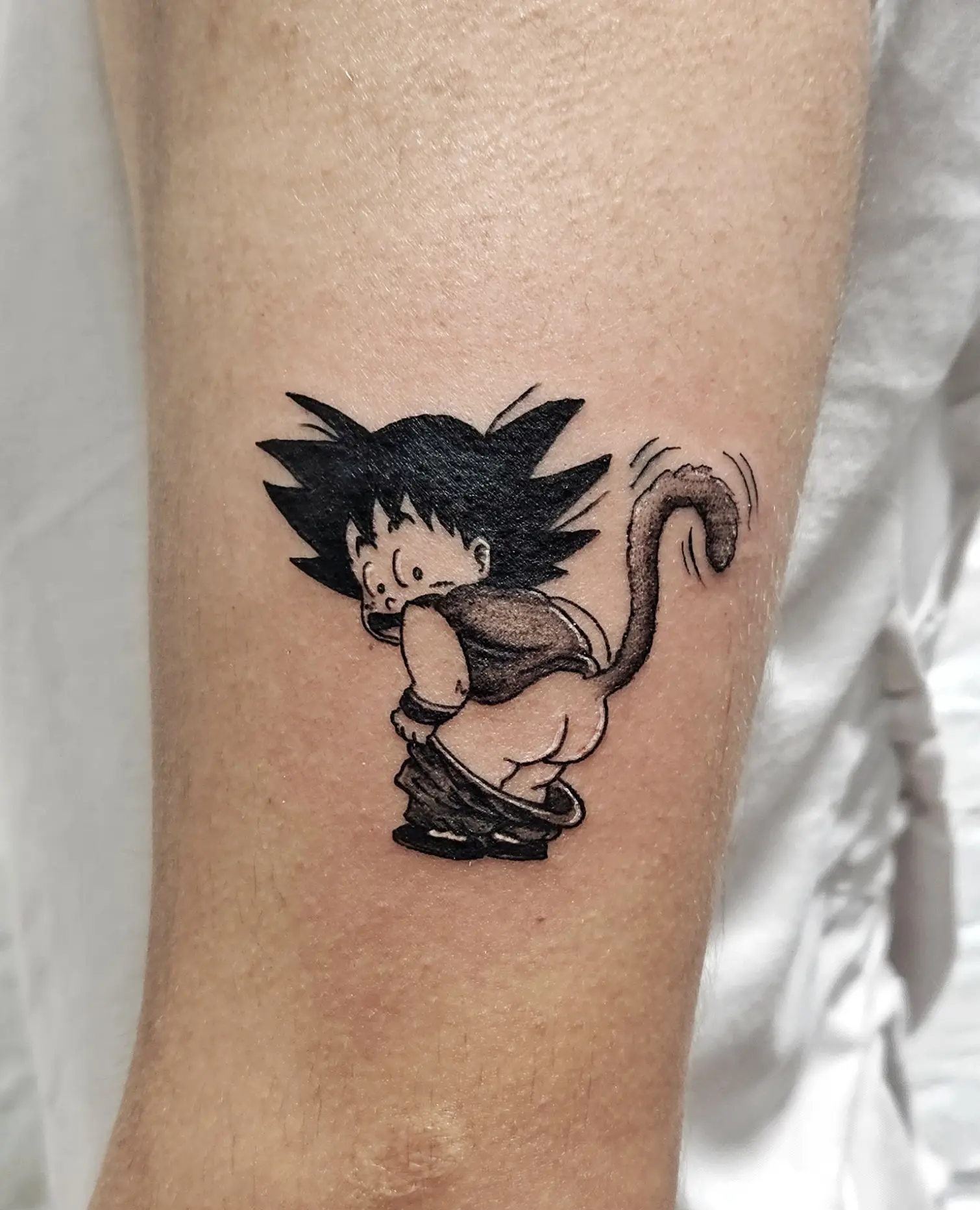 Playful Goku tattoo from Dragon Ball with blackwork shading.