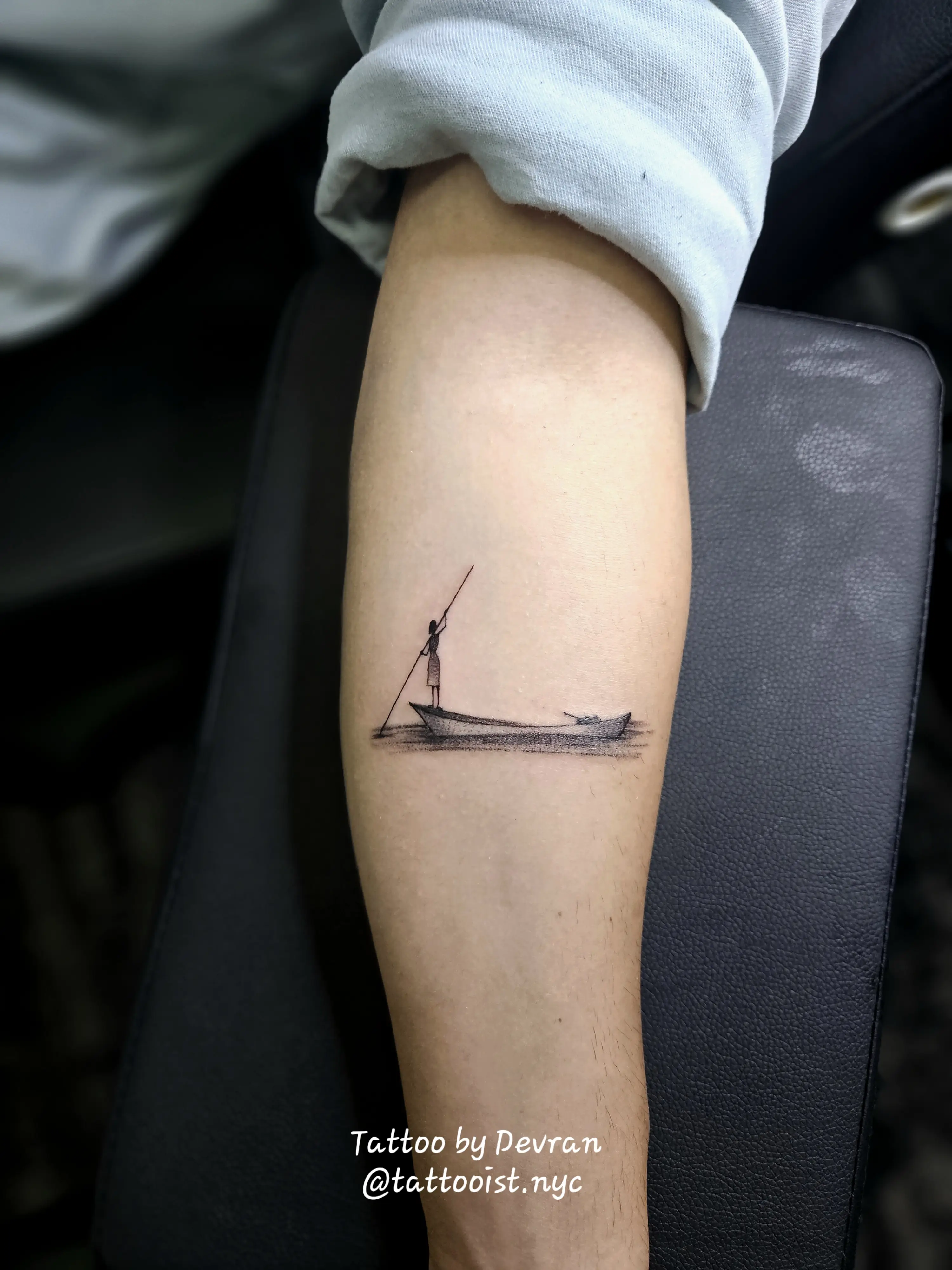 Minimalist fine-line tattoo of a man on a boat, done in delicate black ink.