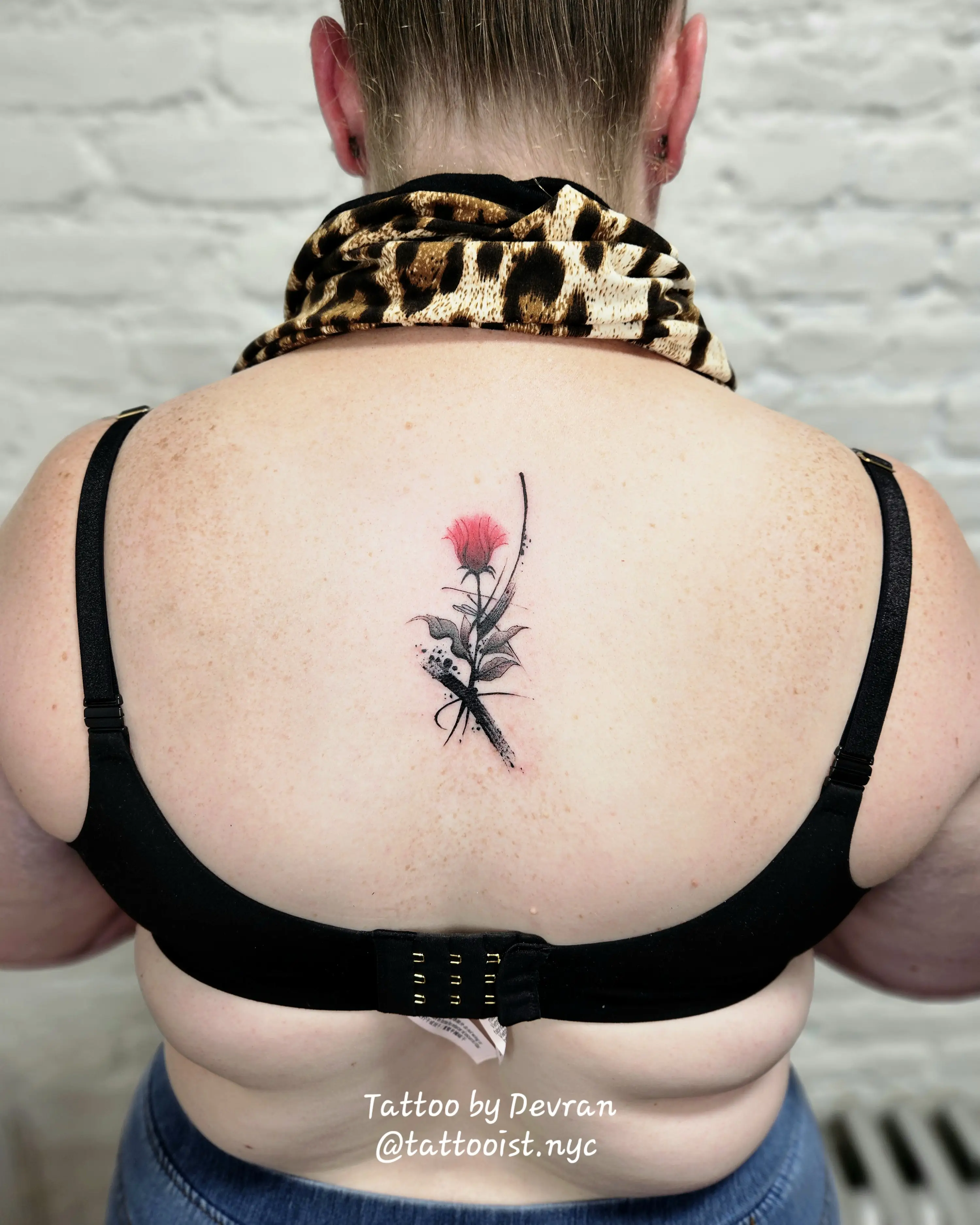 Floral tattoo with red bloom and subtle watercolor effect on the upper back.