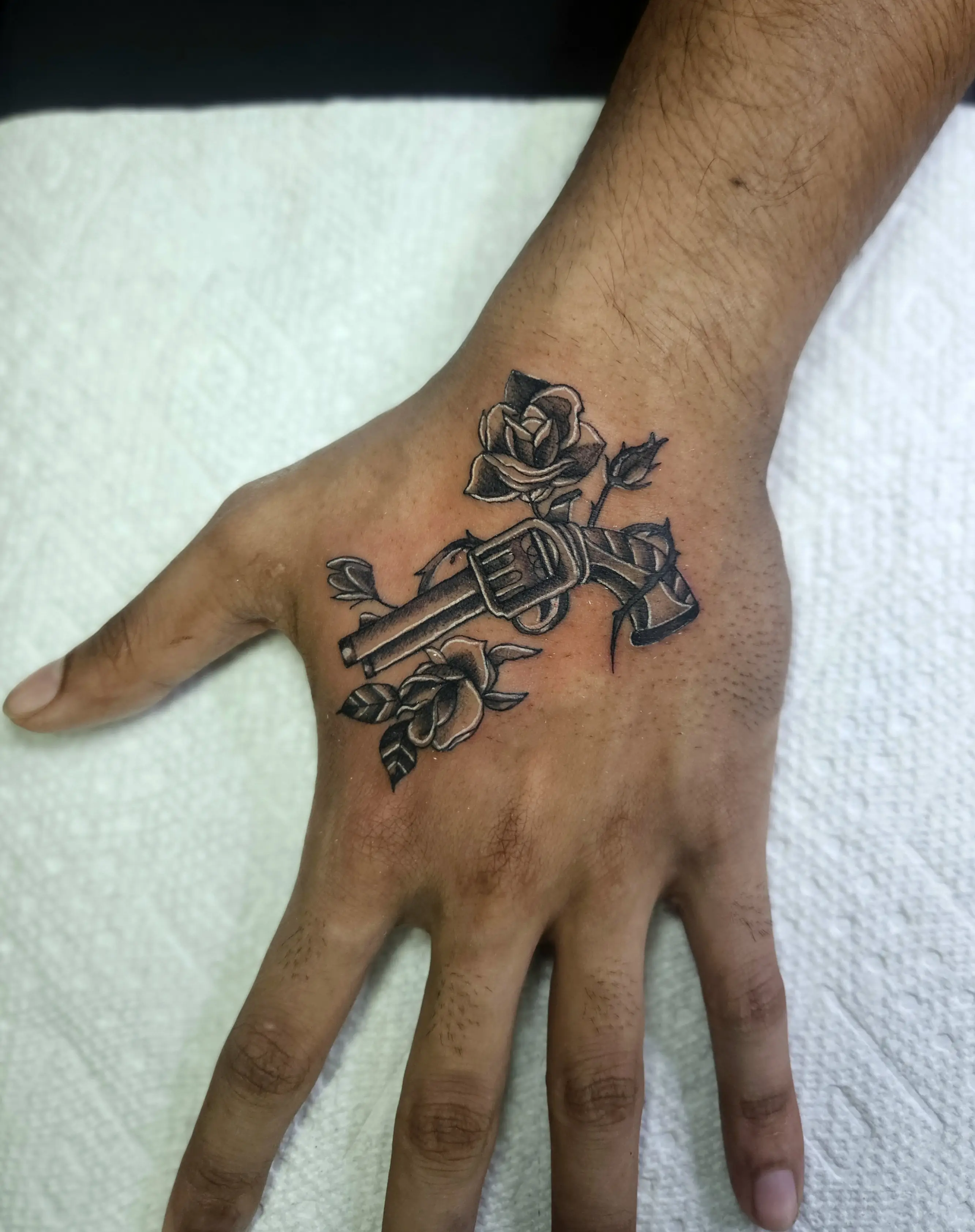 Rose intertwined with a revolver tattoo on the hand in black and gray shading.