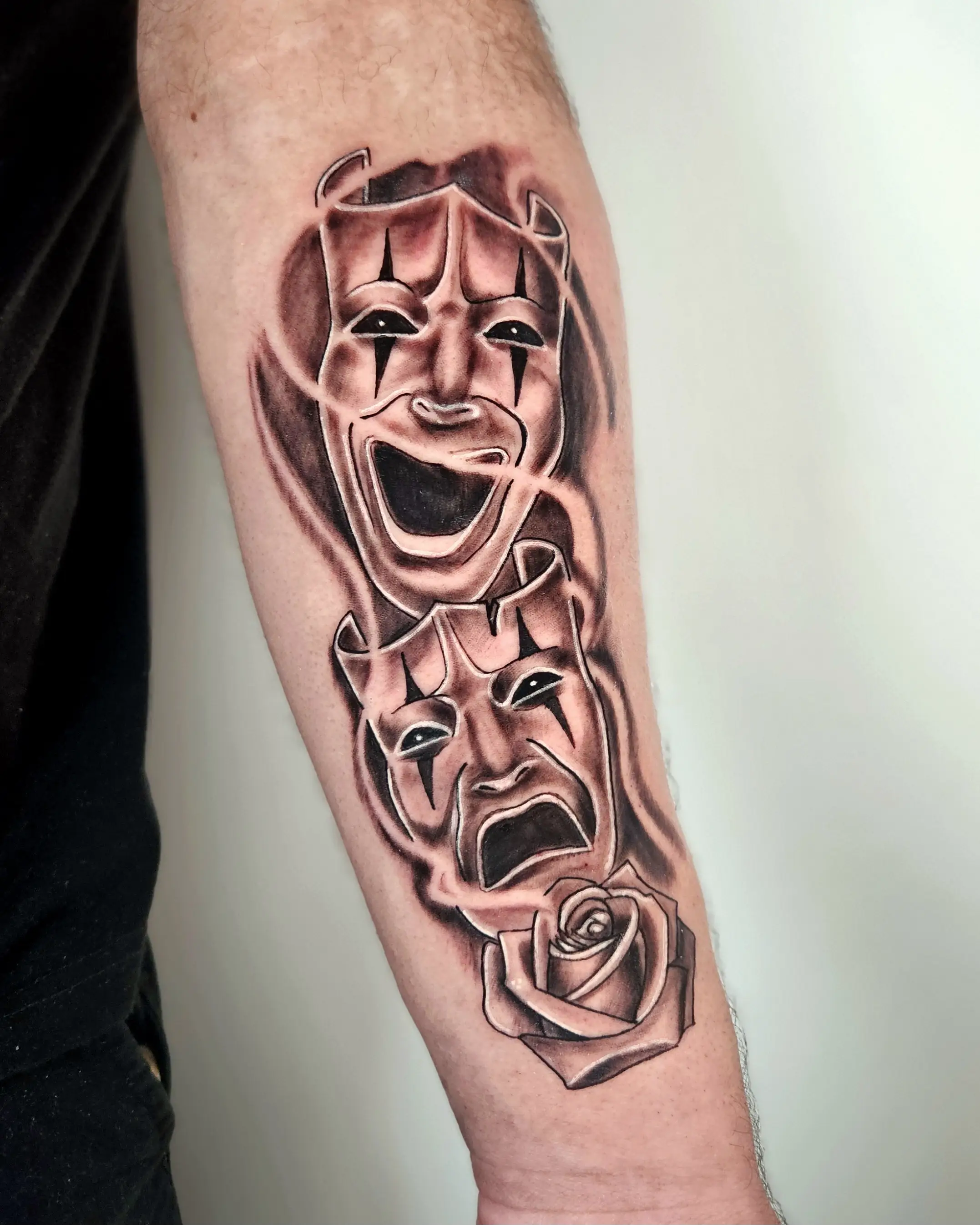 Theatrical comedy and tragedy masks with a rose in black and gray shading.