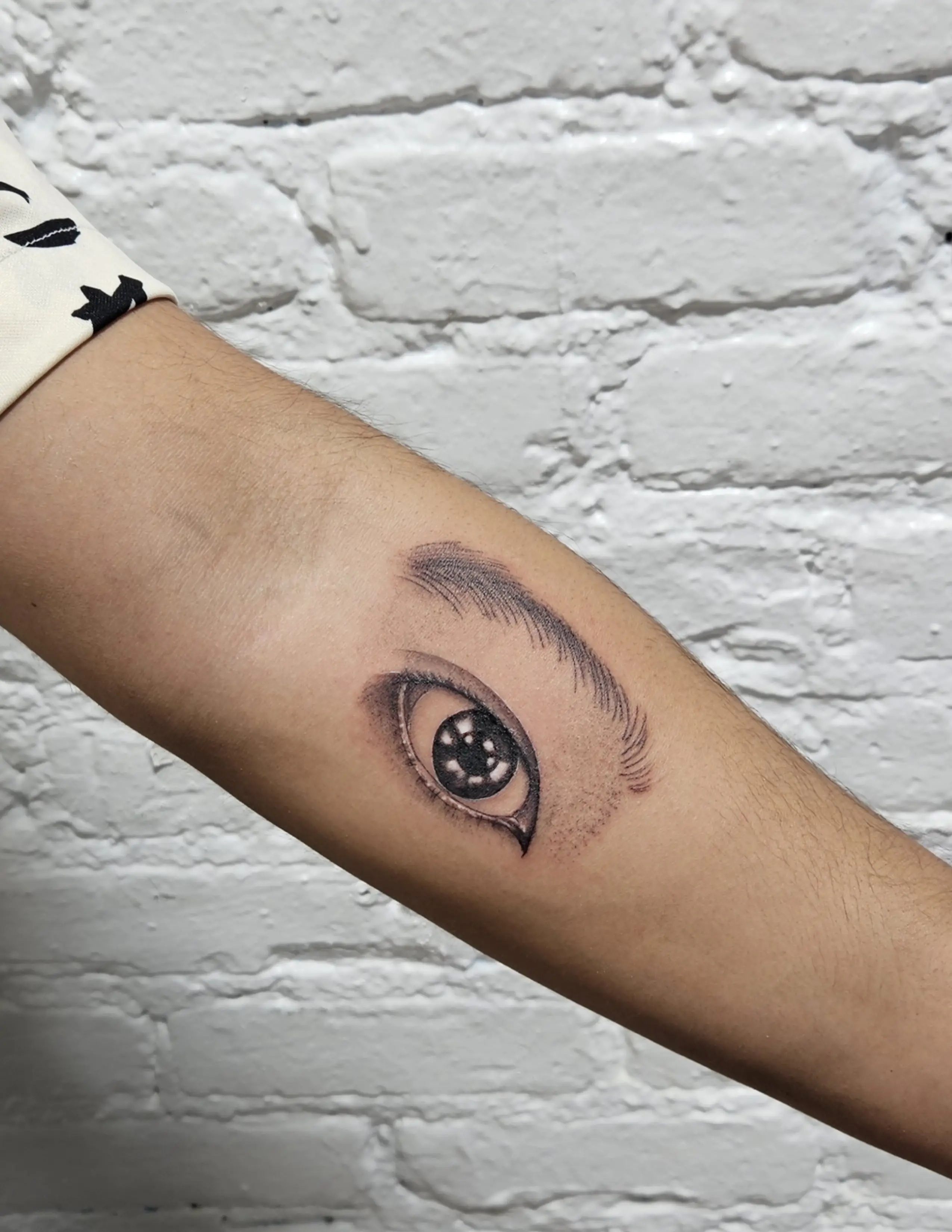 Realistic tattoo of an eye with fine shading on the forearm.