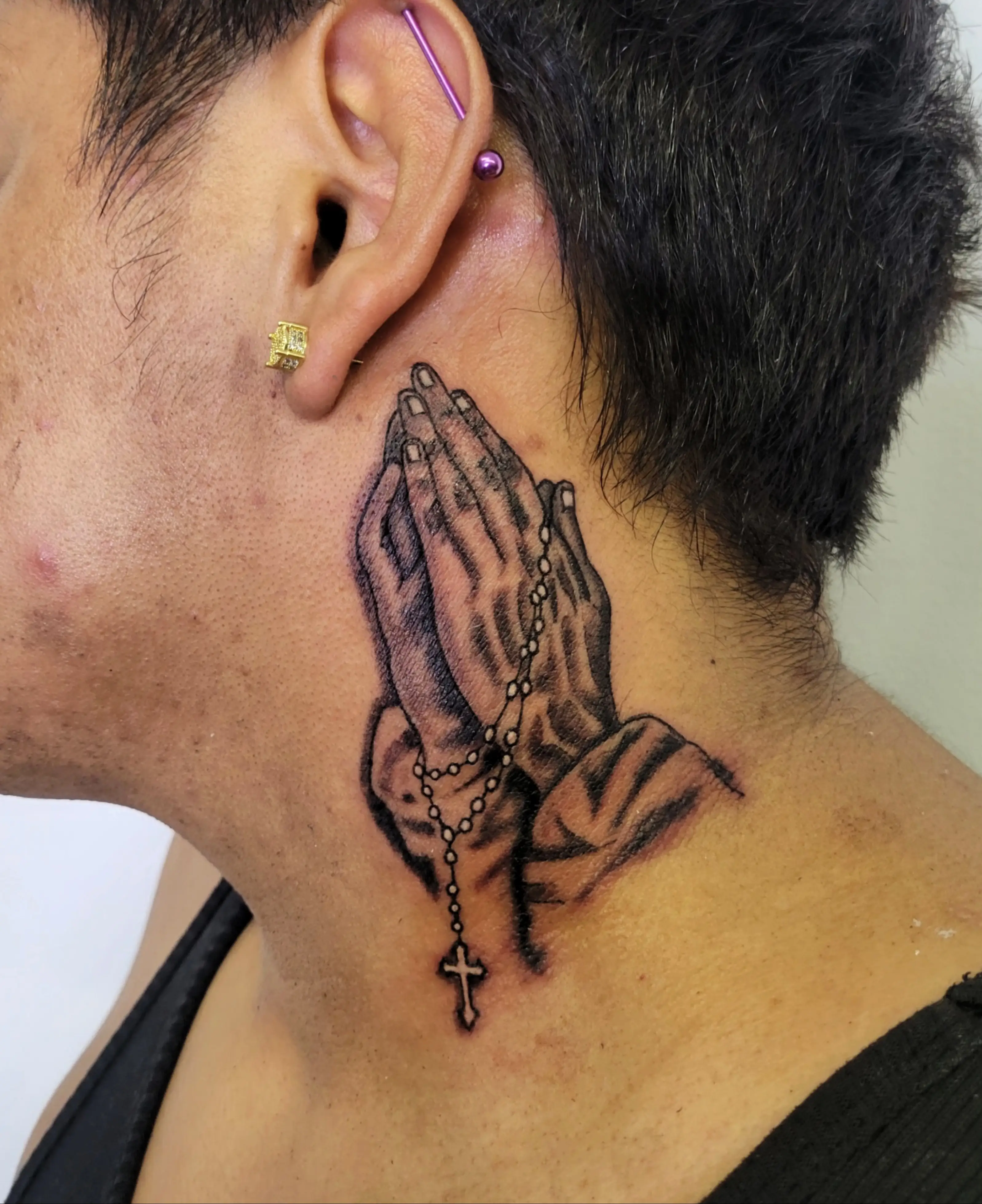Praying hands holding a rosary tattoo on the neck in black and gray realism.