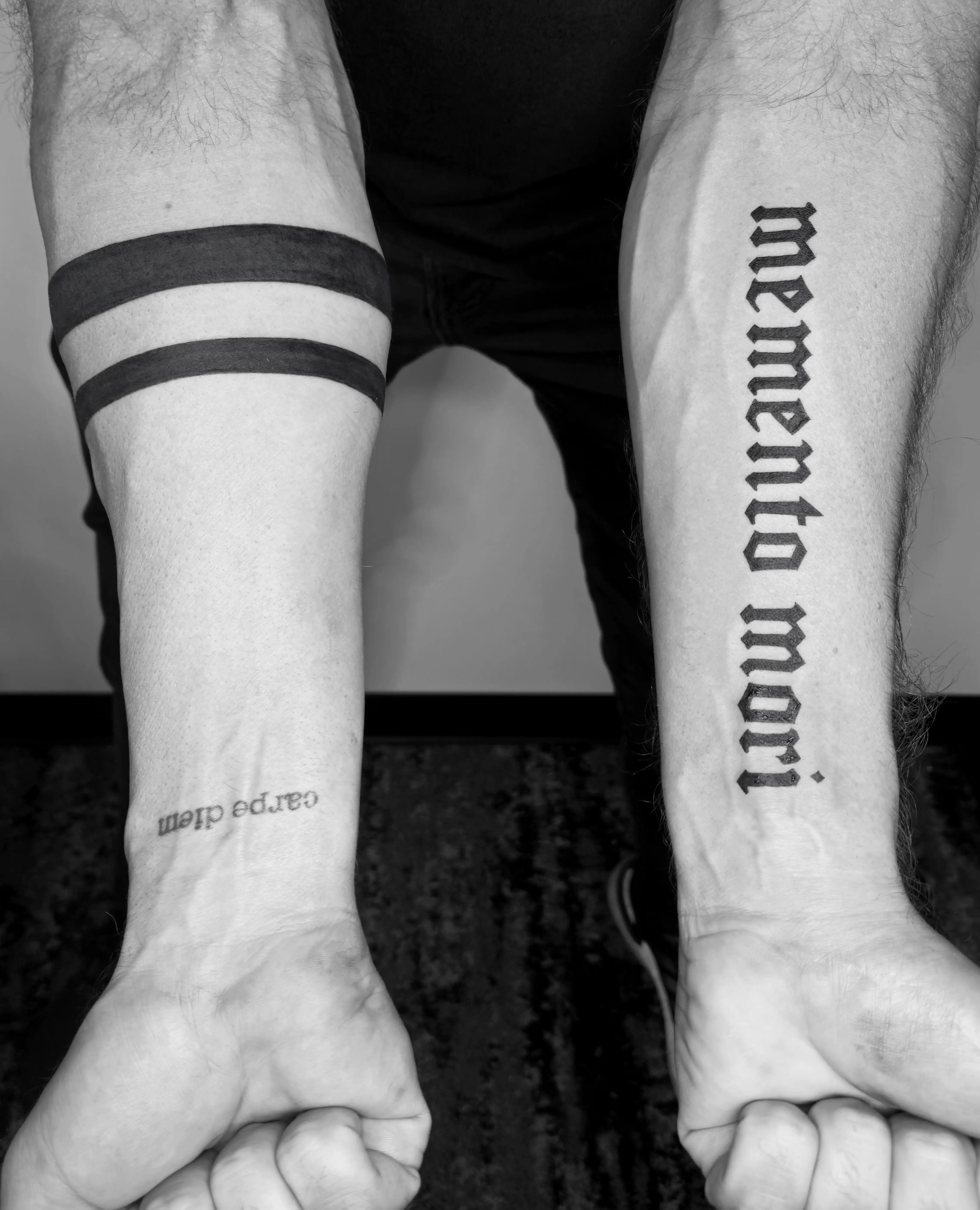 Lettering tattoos 'memento mori' and 'carpe diem' with solid black arm bands.