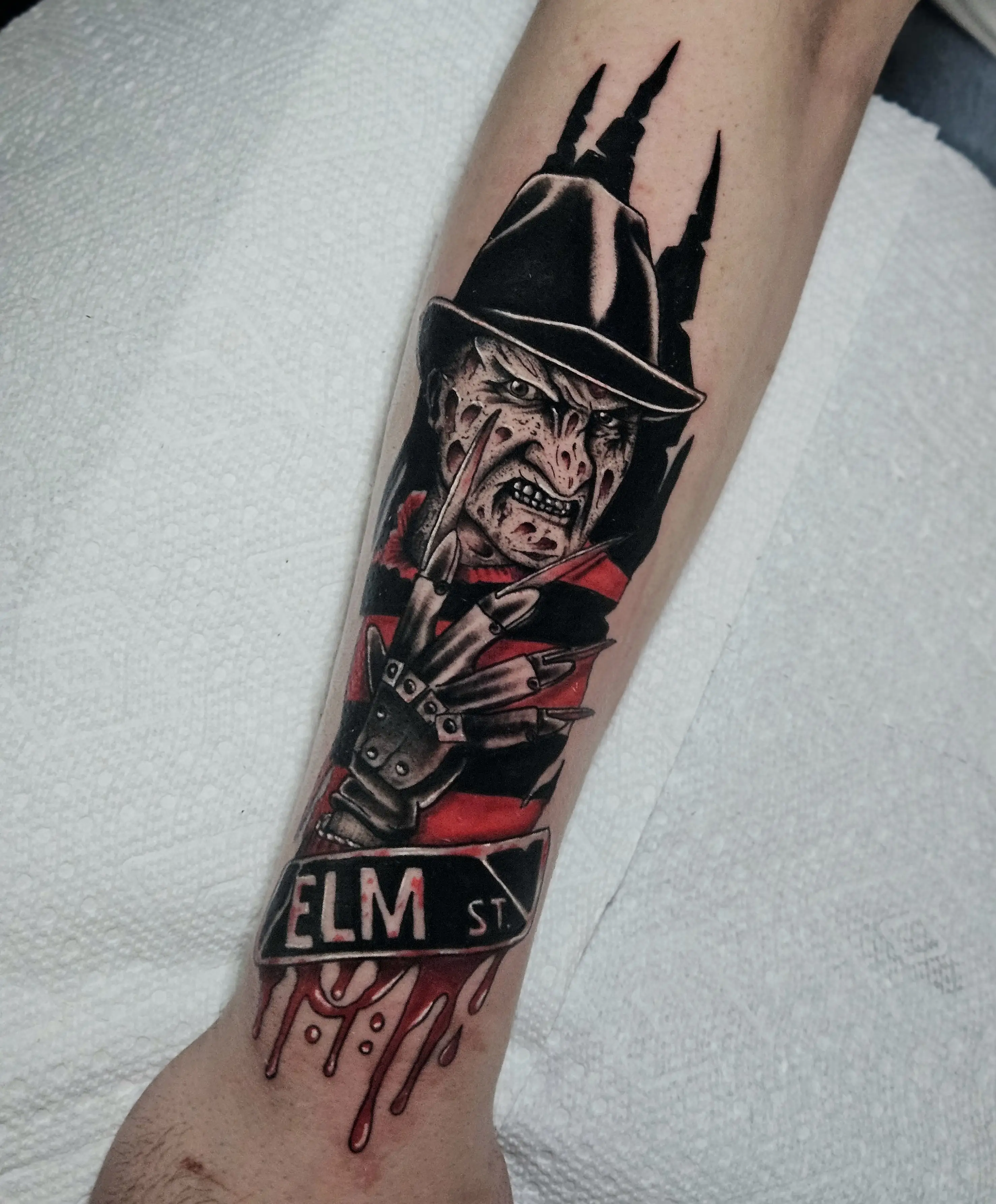 Realistic horror tattoo of Freddy Krueger with 'Elm St.' sign and blood details.