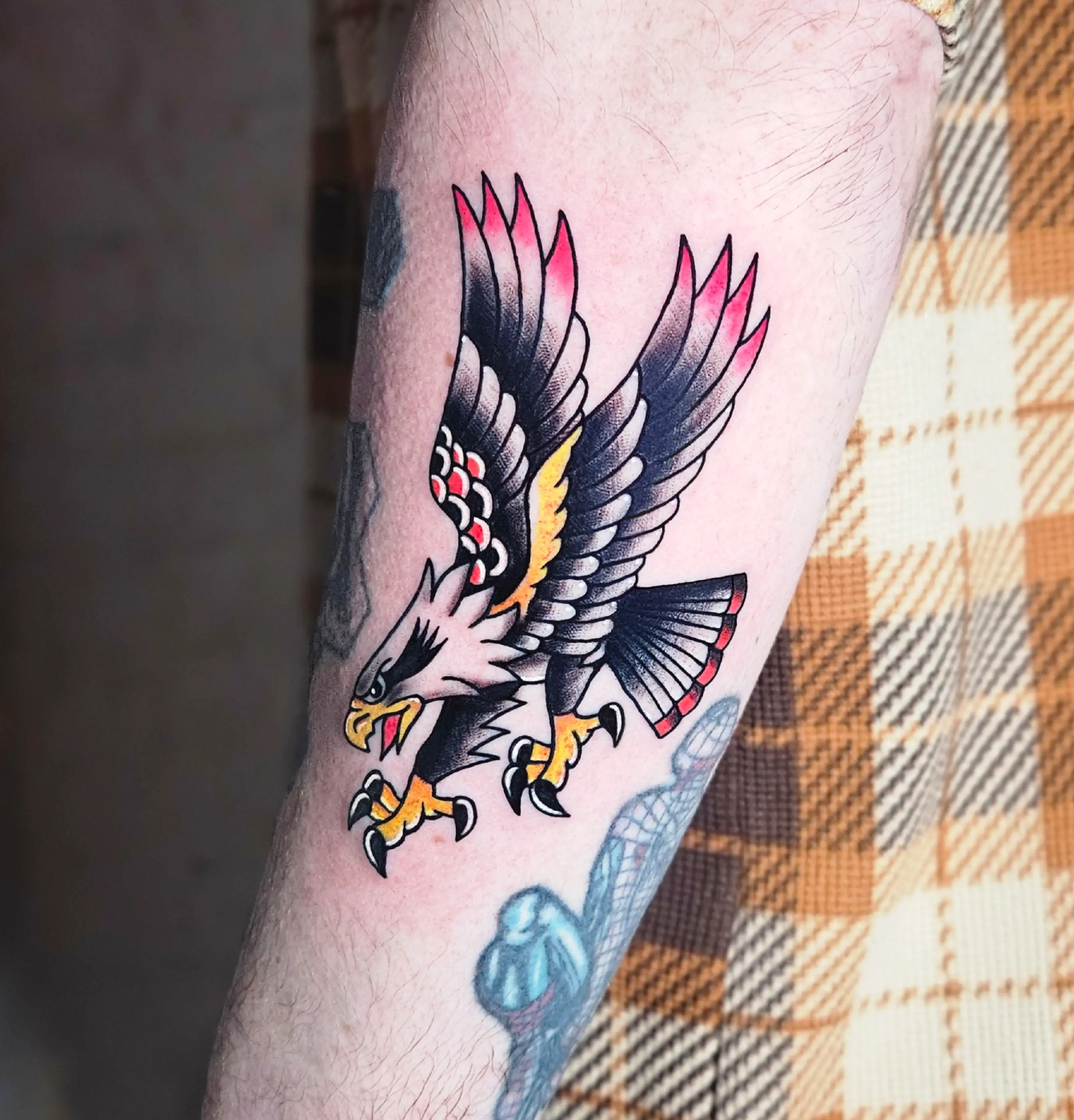 American traditional style eagle tattoo with bold black outlines and vibrant red, yellow, and white highlights.