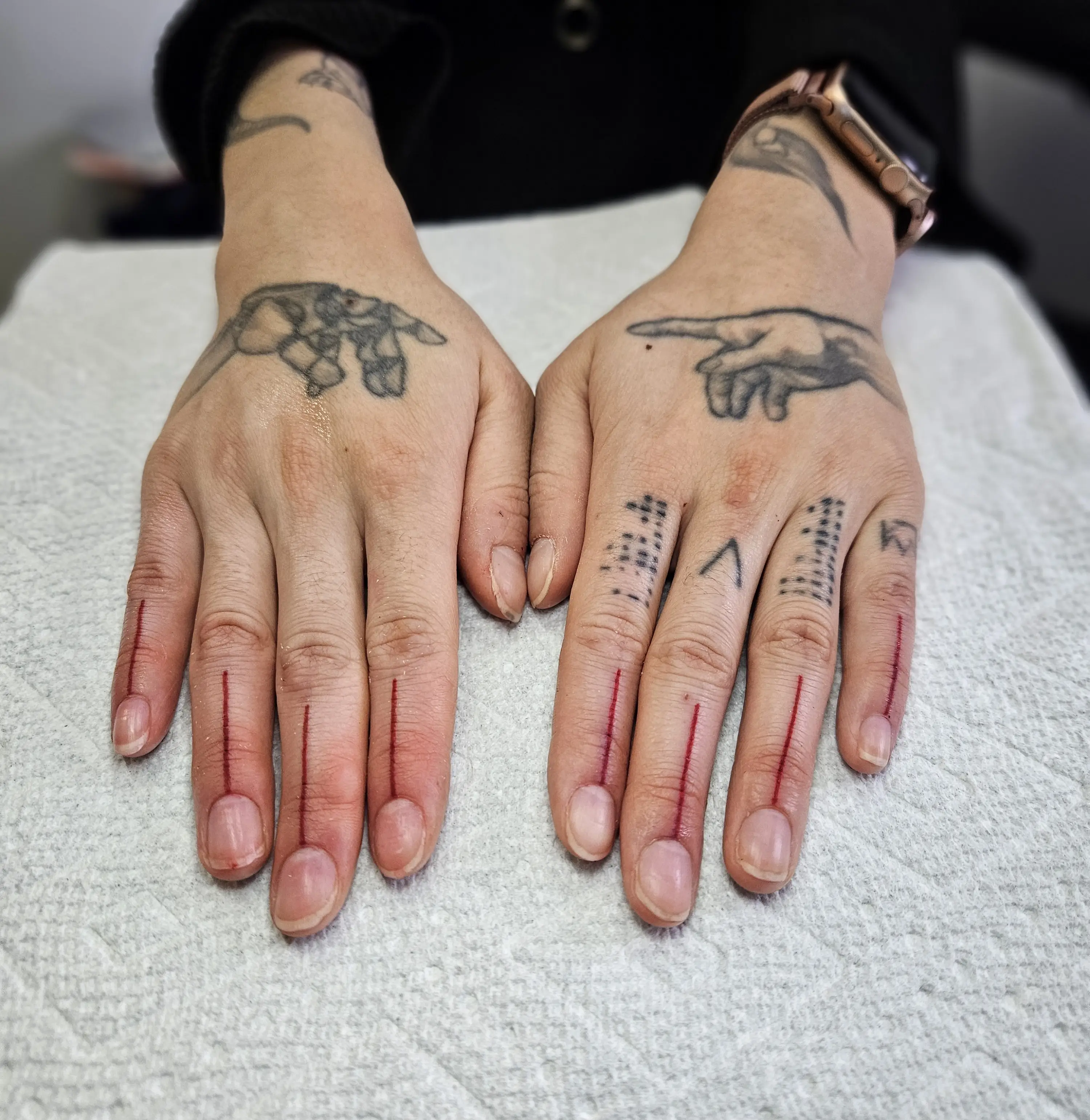 Thin red lines placed on fingers; minimal additions that complement existing hand tattoos.
