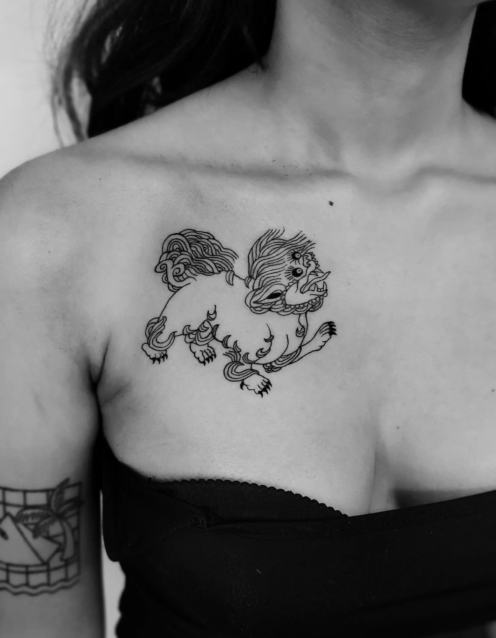A mythological lion-like creature tattoo on the chest/shoulder area. Minimalist design with fine black outlines and detailed linework in sketch style.