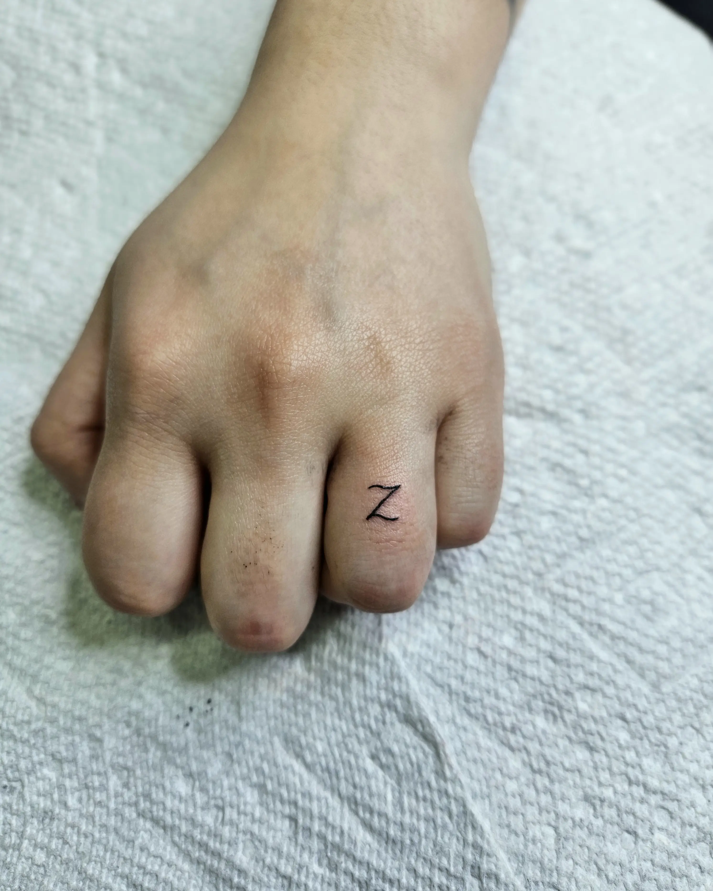Tiny fine line initial tattoo featuring the letter 'Z' placed on the finger.