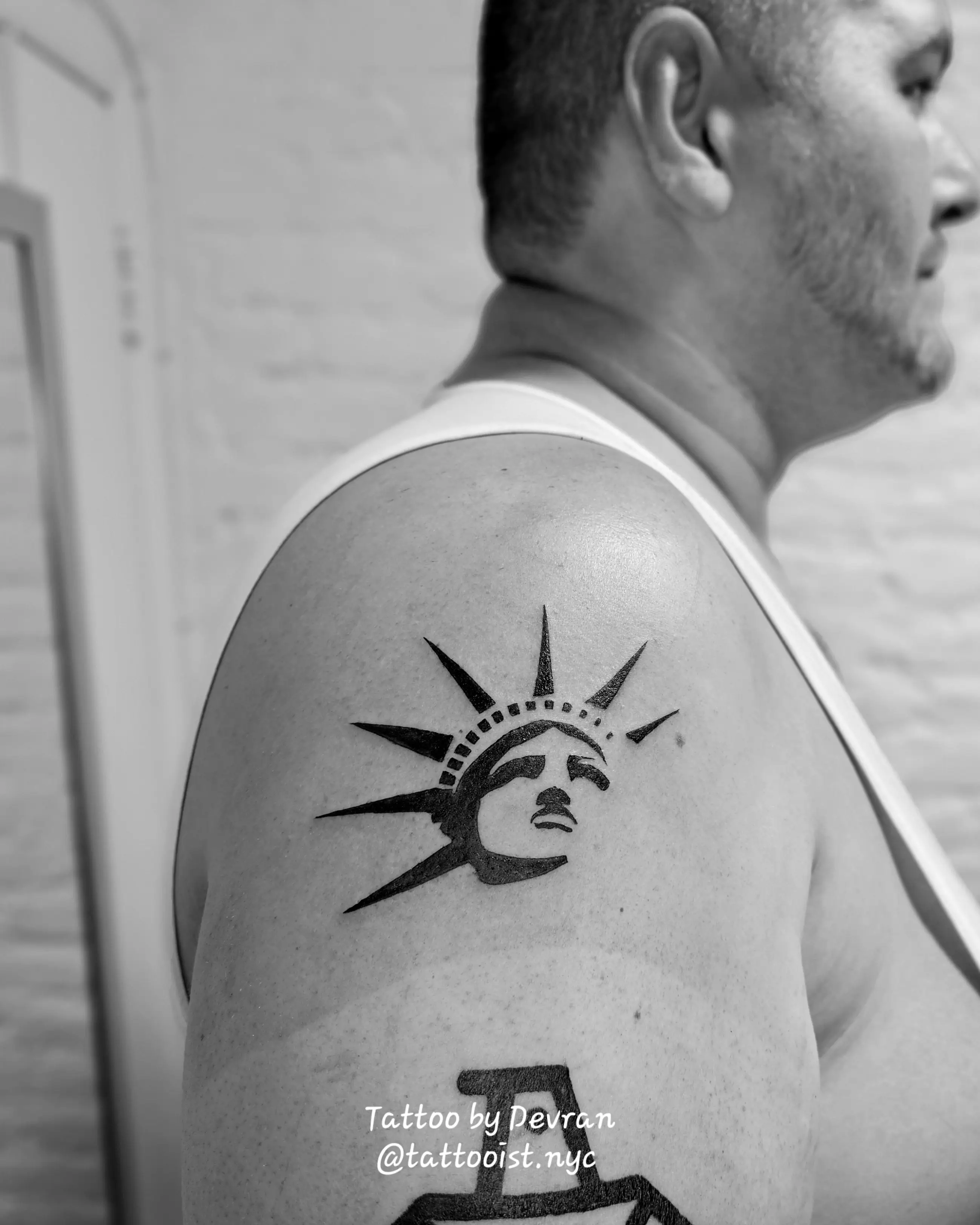 Bold, blackwork tattoo of the Statue of Liberty's head and crown in a stylized, geometric/graphic art style on the upper arm.